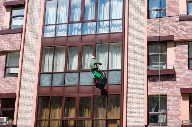 Um homem pendurado em uma corda lava as janelas