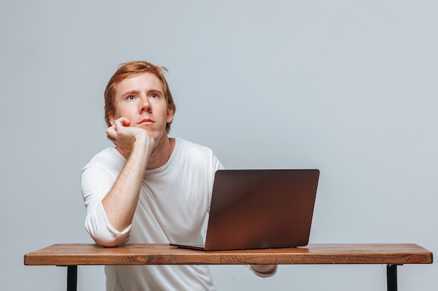 Um homem pensa em um laptop em um fundo claro