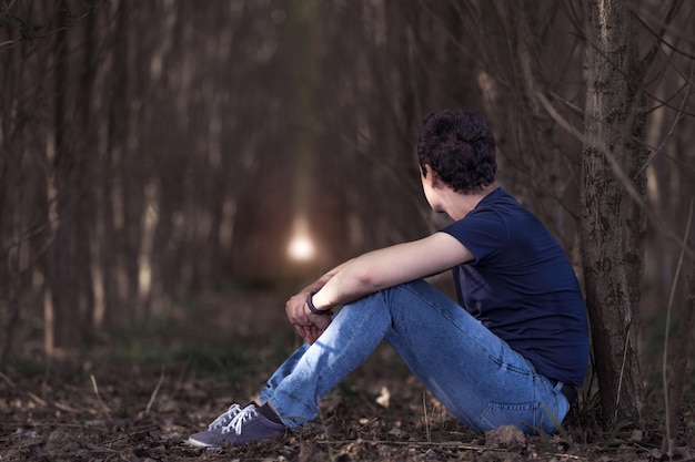 Um homem pensativo na floresta olha para a luz na esperança de tempos melhores. copie o espaço