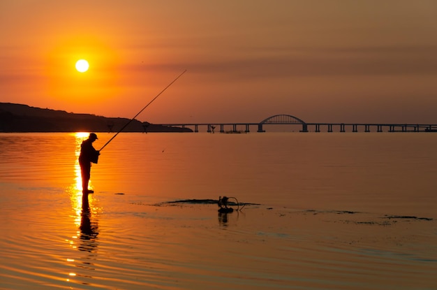 Um homem pescando na água ao pôr do sol