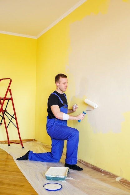 Um homem pinta a parede da casa com um rolo e tinta. remodelação de divisões da casa.