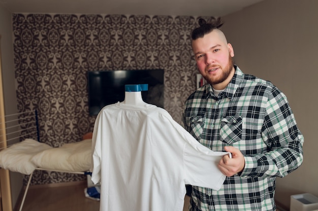 Um homem põe as coisas em ordem segura o vaporizador de roupas na mão e alisa a jaqueta após a lavagem