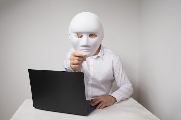 Um homem que trabalha em um laptop cobre o rosto com uma máscara o conceito de anonimato na internet