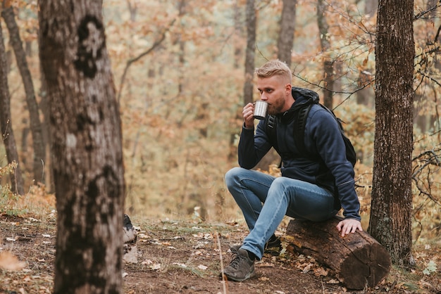 Um homem que viaja na floresta de outono pára e bebe chá.