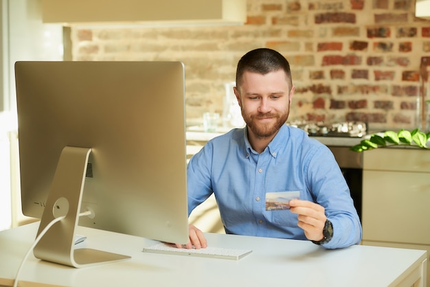 Um homem quer fazer compras on-line e olha para o cartão de crédito em casa.
