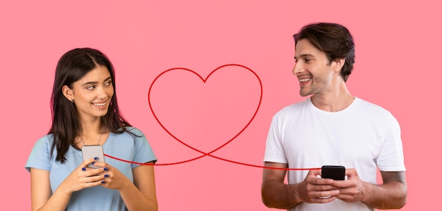 Foto um homem radiante e uma mulher sorridente, ambos de camisas brancas, estão envolvidos com seus smartphones