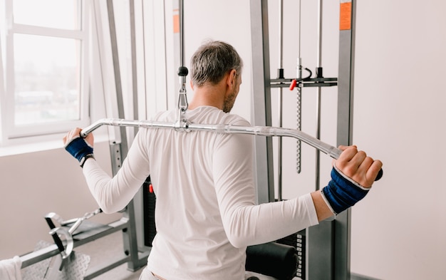 Um homem realiza exercícios no ginásio em um simulador. treinamento de volta. visão traseira