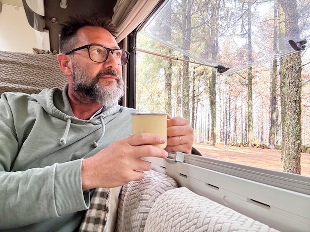 Um homem relaxa e olha pela janela para o parque florestal de dentro de uma caravana de férias vanlife viagem viagem aventura pessoas estilo de vida viajante pessoas aventura nômade