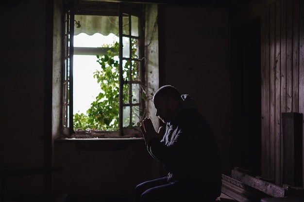 Um homem reza em uma velha casa em ruínas Casa abandonada com uma janela aberta por dentro Conceito de desespero da esperança