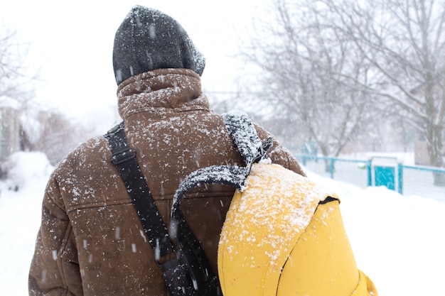 Um homem rústico está andando na rua no inverno com uma mochila amarela. Nevasca de neve