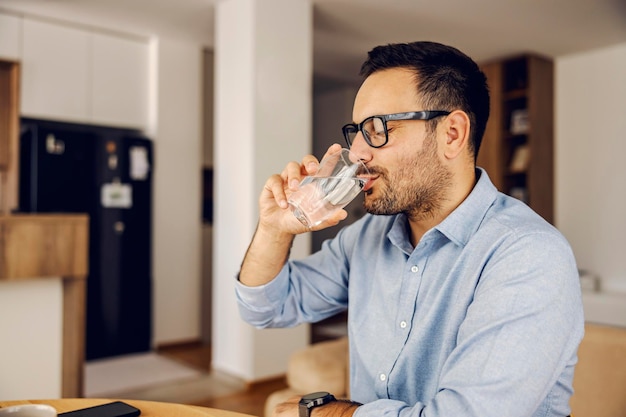 Um homem se senta em casa e bebe um copo de água fresca