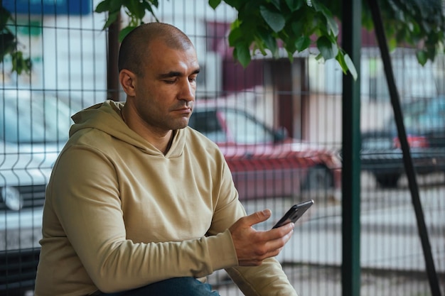 Um homem se senta em um banco no parque e olha pelo telefone