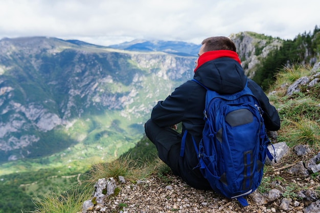 Um homem se senta em um penhasco e olha para a paisagem montanhosa Caminhadas na cordilheira