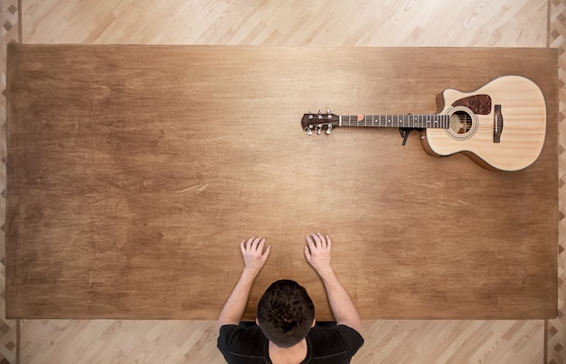 Um homem se senta em uma grande mesa de madeira vazia em que uma guitarra está o espaço da cópia.