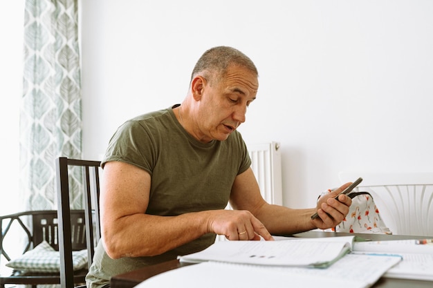 Um homem se senta em uma mesa com uma calculadora e olha para uma calculadora.