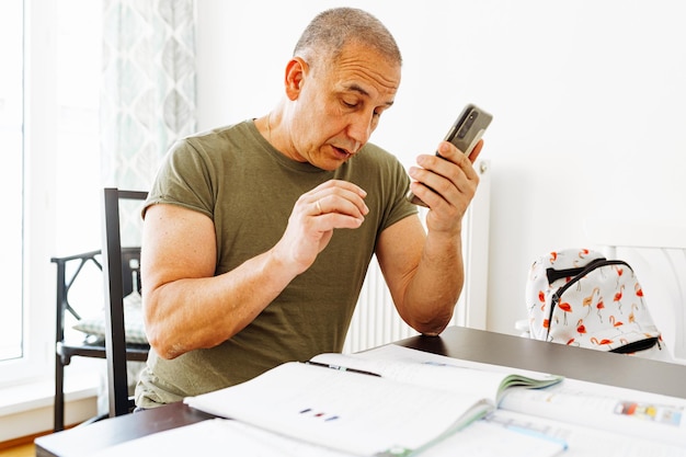 Um homem se senta em uma mesa e olha para o telefone.