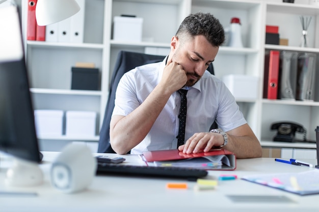 Um homem se senta em uma mesa no escritório e olha para o relógio de pulso.