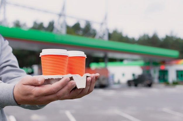 Um homem segura duas xícaras de café em um posto de gasolina.