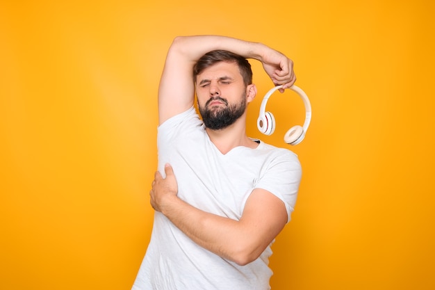 Um homem segura fones de ouvido brancos na mão e fechou os olhos.