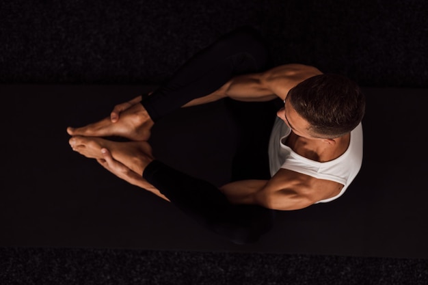 Um homem segura os joelhos com as mãos fazendo ioga vista superior