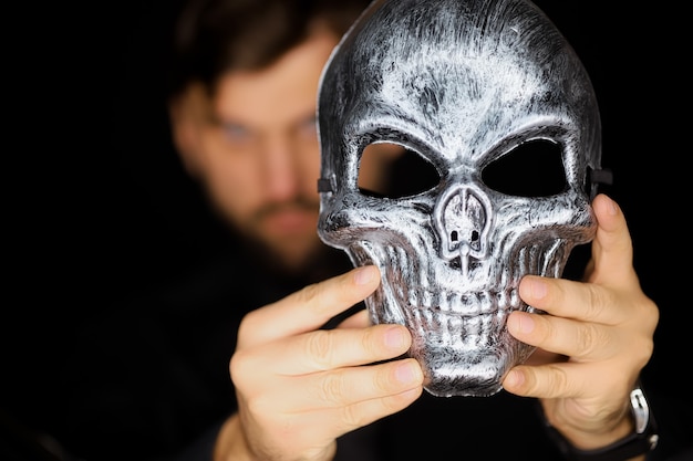 Um homem segura uma máscara de esqueleto na frente dele o que