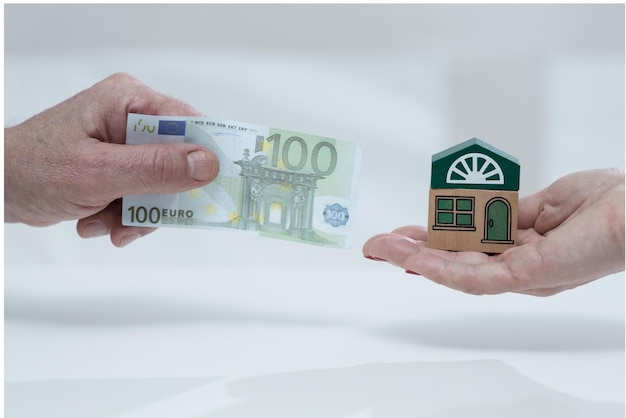 Um homem segura uma pilha de notas de 100 euros em frente a uma casa.