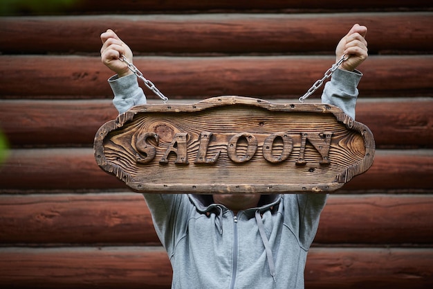 Um homem segura uma placa feita de madeira Saloon