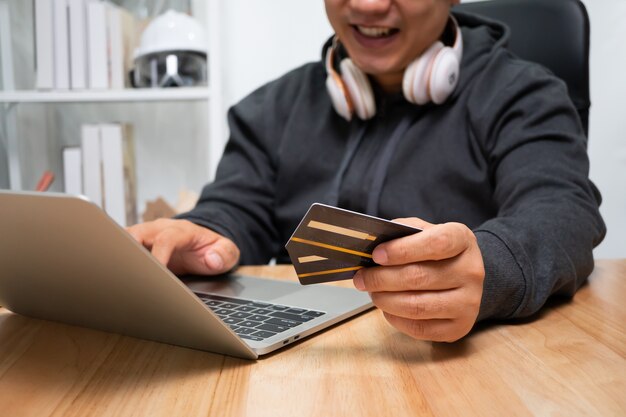 Um homem segurando um cartão de crédito fictício e usando um laptop para pagamento online