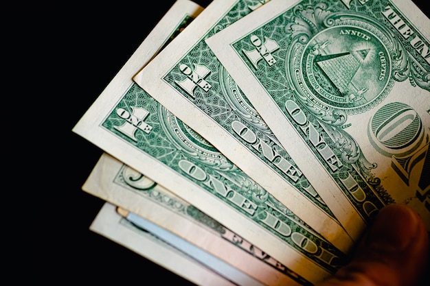 Um homem segurando um maço de notas de dólar americano em uma foto com fundo preto