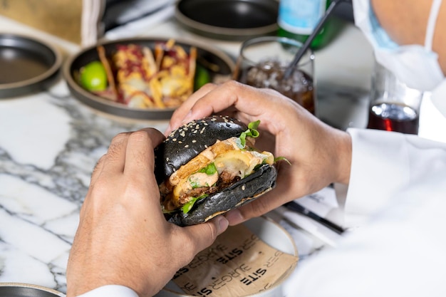 Um homem segurando um sanduíche de hambúrguer de frango preto e vai comê-lo