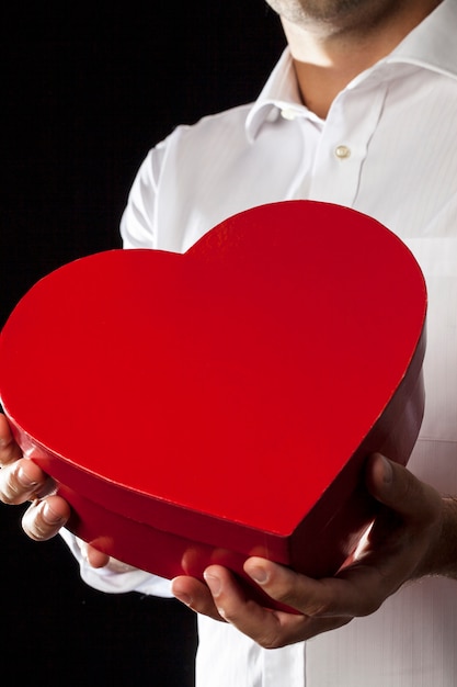 Foto um homem segurando uma caixa de presente de coração em um gesto de doação.