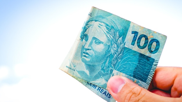 Um homem segurando uma nota de 100 reais brasileiros