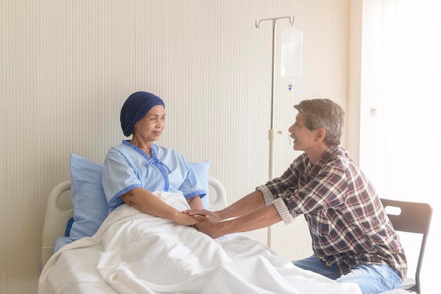 Um homem sênior visitando mulher paciente com câncer usando lenço na cabeça no hospital