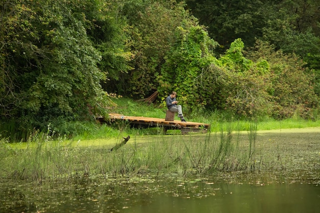 Um homem senta-se em uma doca de barco de madeira em um lago da floresta.