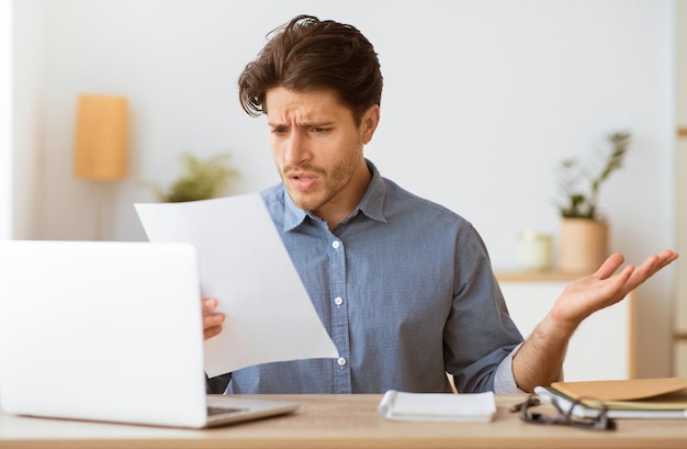 Um homem senta-se em uma mesa com uma expressão confusa enquanto lê um documento ele está olhando para o documento