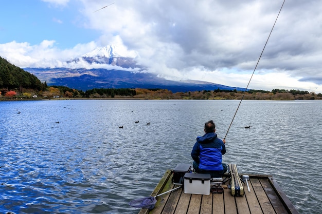 Um homem sentado e pescando sozinho na ponte de madeira no lago Kawaguchiko no Japão durante o pôr do sol com Fuji