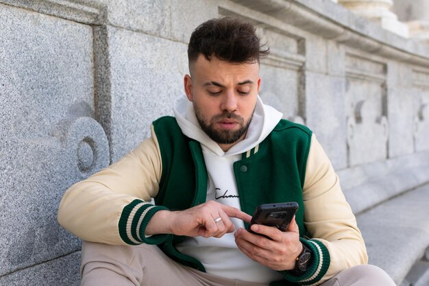 Um homem sentado em uma parede usando seu telefone