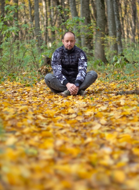 Um homem sentado na floresta no fundo da folha cai em um dia ensolarado de outono na Rússia