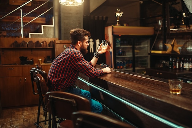 Um homem sentado no balcão do bar e bebe bebida alcoólica. Homem em pub