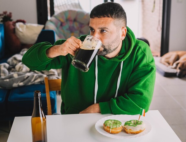 Um homem solteiro comendo rosquinhas e cerveja preta no café da manhã para comemorar o Dia de São Patrício