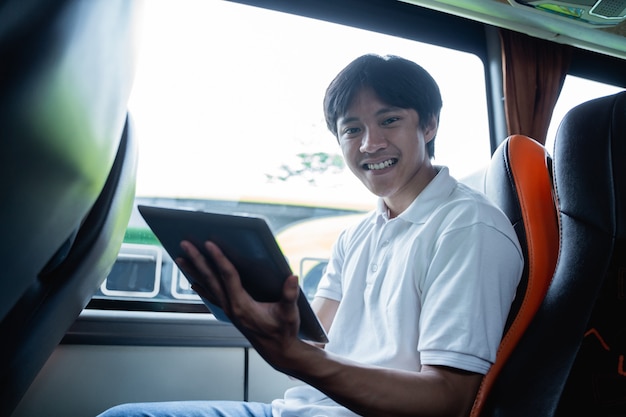 Um homem sorri enquanto usa um bloco enquanto está sentado em um ônibus