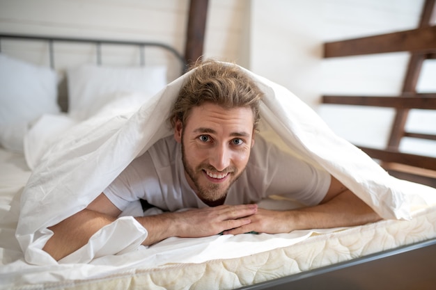 Foto um homem sorridente se cobrindo com um cobertor