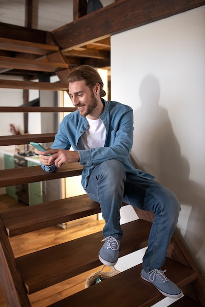 Um homem sorridente trocando mensagens de texto com um amigo enquanto está sentado na escada