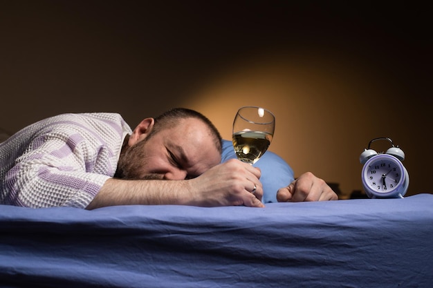 Um homem sozinho com uma taça de vinho na cama Alcoolismo solidão Beber álcool para dormir Um quarto escuro