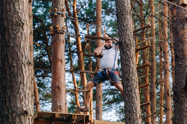 Um homem supera um obstáculo em uma cidade de cordas Um homem em um parque de cordas na floresta