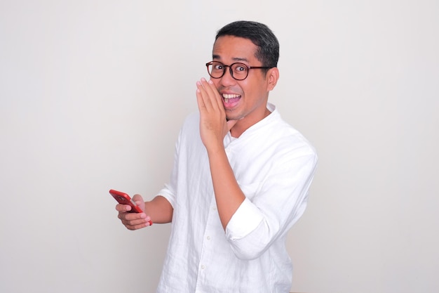 Um homem sussurrando algo com expressão feliz enquanto segura um telefone celular