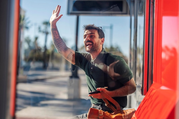 Um homem tatuado feliz está sentado em uma estação e parando um táxi na rua da cidade