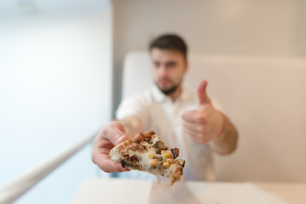 Um homem tem um pedaço de pizza nas mãos e mostra o dedo na entrada. um homem gosta de pizza. gostar.