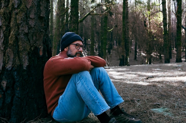 Um homem tendo tempo de relaxamento sentado no chão no meio de florestas verdes e ao ar livre relaxando atividade de lazer pessoas e amor sentimento com parque natural bem-estar estilo de vida alternativo