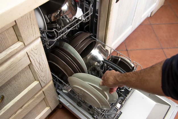 Um homem tirando pratos de uma máquina de lavar louça. Conceito de viver solteiro.